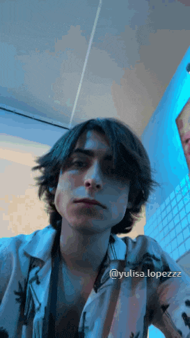 a young man with long hair is taking a selfie in a room with a blue light behind him .