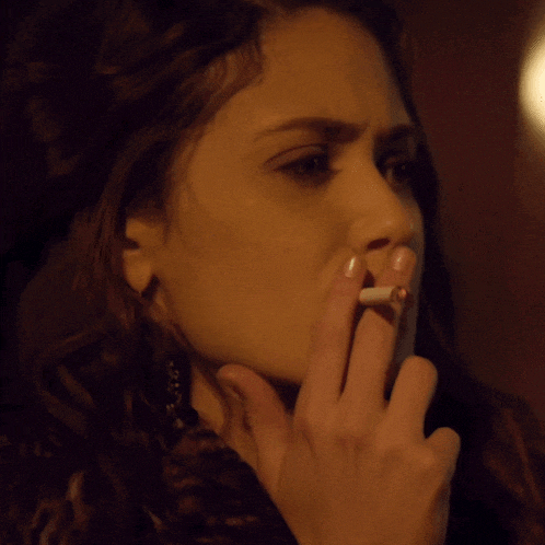 a close up of a woman smoking a cigarette in a dark room