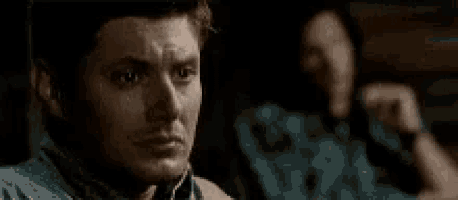a man is making a funny face in a dark room while another man sits behind him .