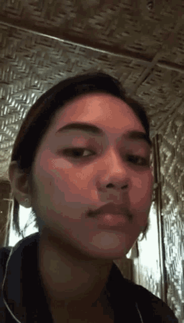 a close up of a woman 's face with a bamboo ceiling behind her .