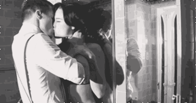 a man and a woman are kissing in front of a mirror in a bathroom .