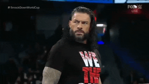 roman reigns is wearing a black t-shirt with the word we on it while standing on a stage .