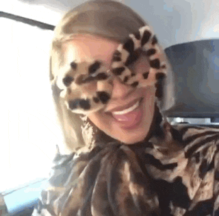 a woman wearing leopard print sunglasses and a leopard print shirt is smiling and sticking her tongue out .