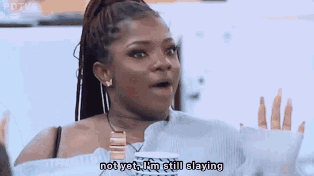 a woman is sitting at a table with a cup of coffee and says " not yet i 'm still slaying "