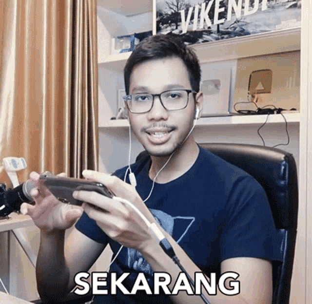 a man wearing glasses and ear buds is holding a cell phone and the word sekarang is on the bottom