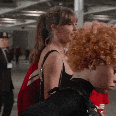 a woman with red curly hair is standing next to another woman in a black dress