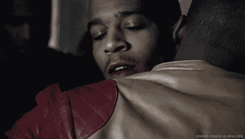 a man in a leather jacket is hugging another man with his eyes closed .