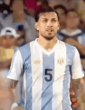 a man in a striped soccer jersey with the number 5 on it is standing in front of a crowd .