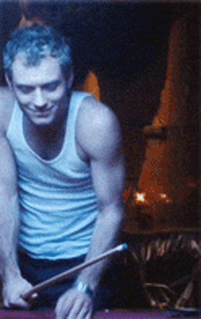 a man in a white tank top holds a pool cue