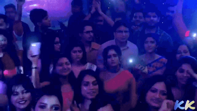 a crowd of people are dancing in a dark room with kk written on the bottom right