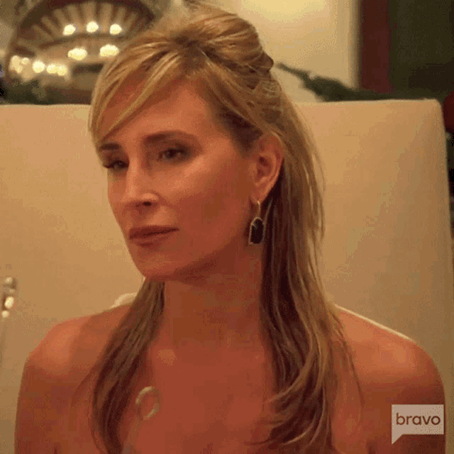 a woman wearing earrings and a necklace is sitting in front of a bravo logo