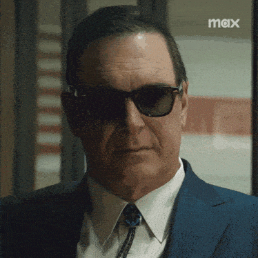 a man in a suit and tie wearing sunglasses with a max logo in the corner