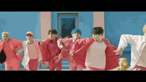 a group of young men in pink clothes are dancing in front of a blue wall