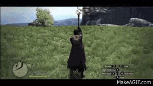 a man in a red cape is standing in a field in a video game holding a staff .