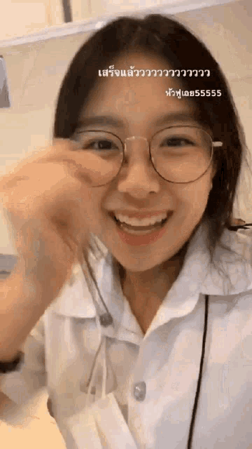 a woman wearing glasses and a white shirt is smiling and holding her nose