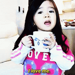 a little girl wearing a shirt that says i love me is holding a cup