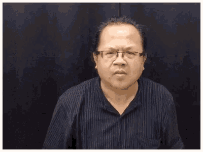 a man wearing glasses and a striped shirt is making a funny face while waving his hand .