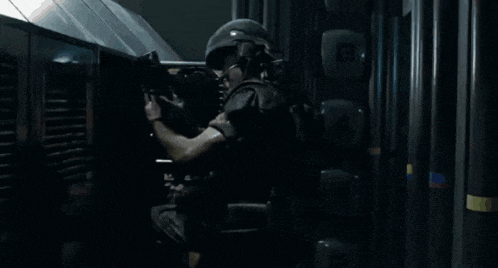a group of soldiers are standing in a dark room and one of them is wearing a helmet .