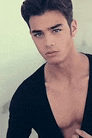 a young man without a shirt is standing in front of a wall and looking at the camera .