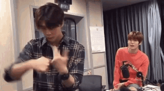 a man in a plaid shirt is standing next to a man in a red shirt in a room .