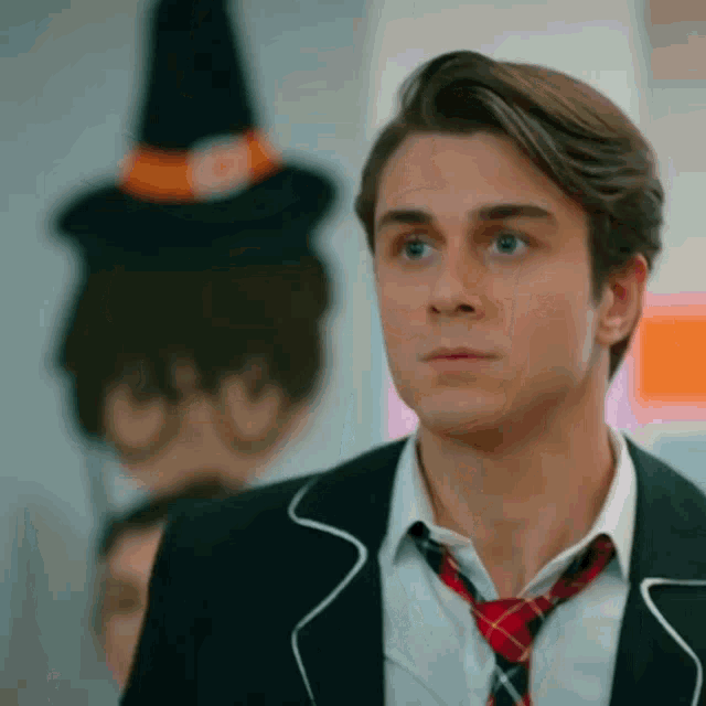 a young man in a suit and tie is standing in front of a painting of a witch hat .