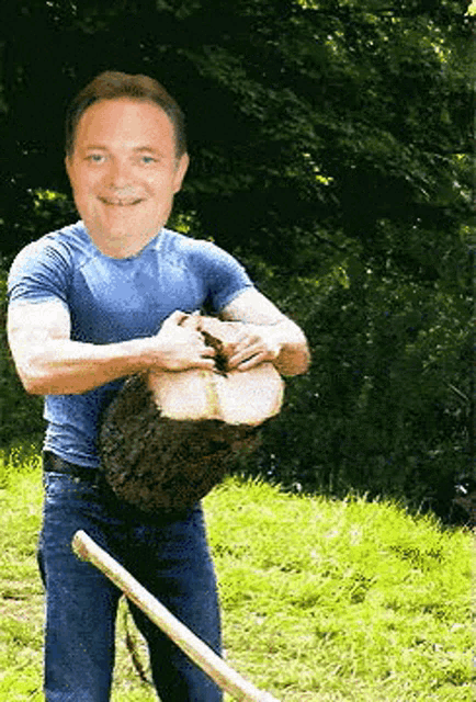 a man in a blue shirt is holding a large piece of wood in his hands