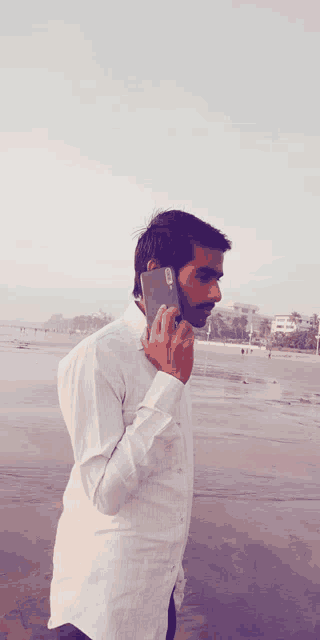 a man in a white shirt is talking on a cell phone on a beach