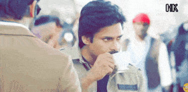 a man with a mustache is drinking from a cup with hk written in the corner