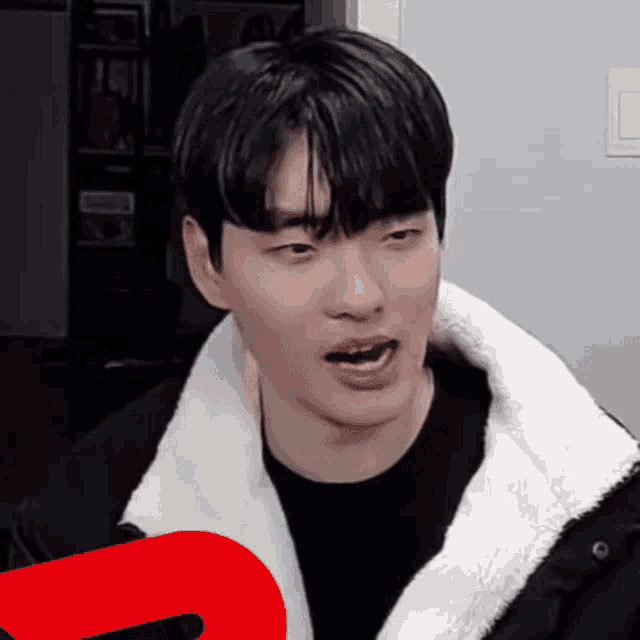 a young man wearing a black shirt and a white jacket is making a funny face with his mouth open .