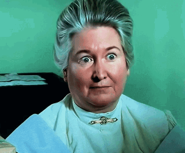 an older woman wearing a white shirt with a gold brooch around her neck