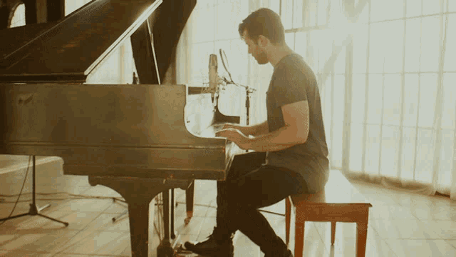 a man sits on a bench playing a piano in front of a window