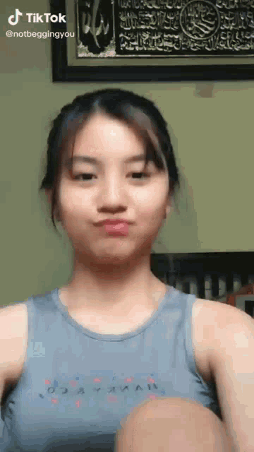 a girl in a tank top is making a funny face in front of a framed picture .