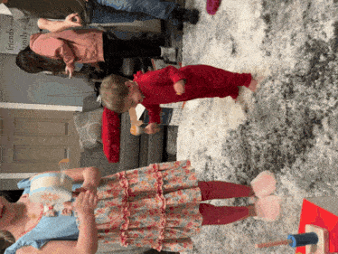 a little girl in a floral dress stands next to a little boy in a red onesie