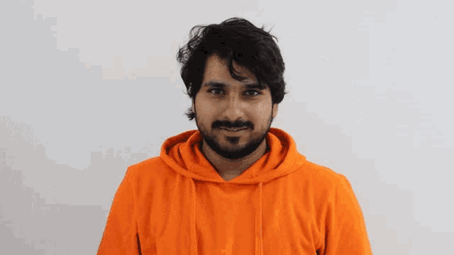 a man wearing an orange hoodie and a watch covers his eyes with his hands