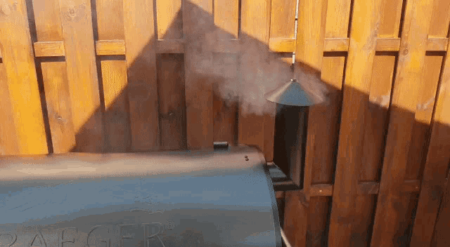 smoke is coming out of a traeger grill against a wooden fence