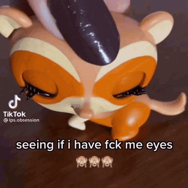 a littlest pet shop toy is sitting on a wooden table with its eyes closed and a person holding it .
