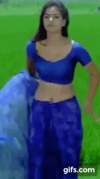 a woman in a blue crop top and blue pants is standing in a grassy field .