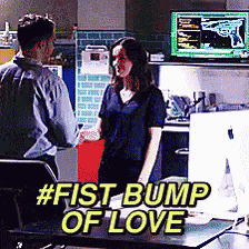 a man and a woman are standing next to each other in front of a computer monitor with the caption # fist bump of love .