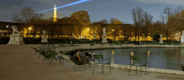 a man sits in a chair near a pond in a park