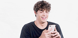 a man with curly hair is laughing while holding a cell phone .