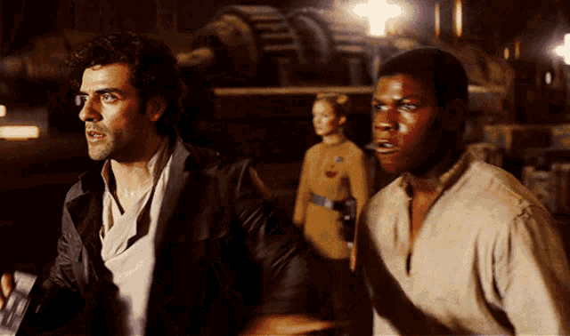 two men standing next to each other in a dark room with a woman in the background