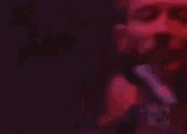 a man is singing into a microphone in a dark room with a red light behind him .