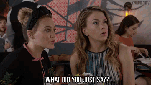 two women are sitting at a table in a restaurant and one of them is asking what did you just say
