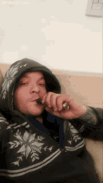 a man in a hoodie is smoking an electronic cigarette with mp4togif.com in the corner