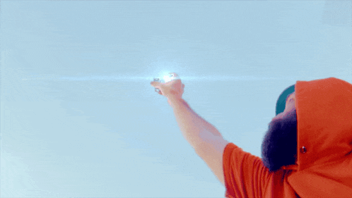 a man with a beard wearing an orange shirt and a green hat is holding something in his hand against a blue sky
