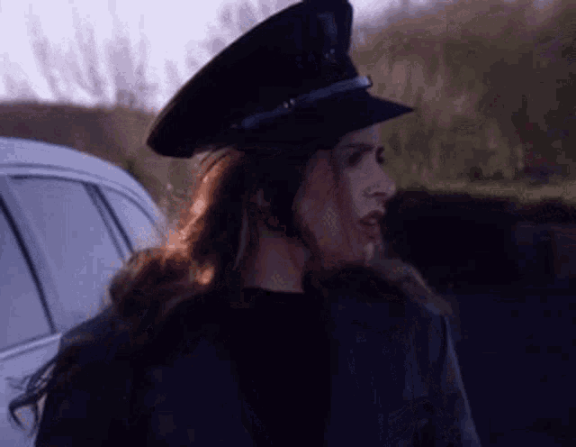 a woman wearing a police hat is standing in front of a white car .