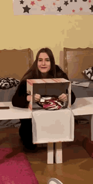 a woman is kneeling down in front of a cardboard box holding a pair of shoes .