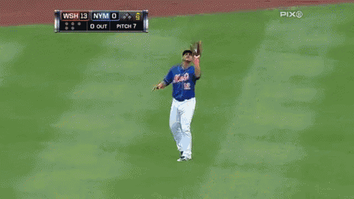 a mets player stands on the field looking at the ball