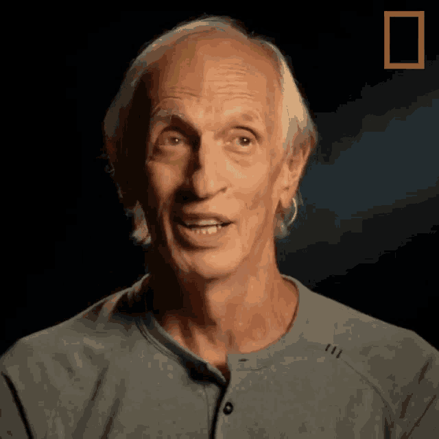 a man in a grey shirt is smiling in a dark room