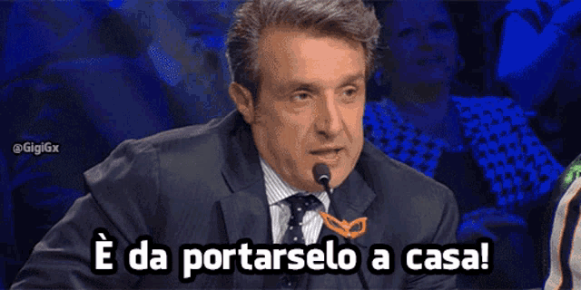 a man in a suit and tie speaking into a microphone with the words e da portarselo a casa